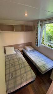 two beds in a small room with a window at Chaleureux Mobil Home in Ivry-la-Bataille