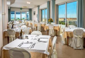 a restaurant with white tables and chairs and windows at Hotel Astoria in Cervia
