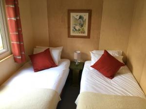 two beds with red pillows in a room at Woodland Cabins, Glencoe in Ballachulish