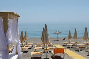 a beach with tables and chairs and umbrellas at Hotel Sylesia in Letojanni