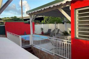 a red house with a white fence and a porch at Appartement d'une chambre avec piscine privee jardin clos et wifi a Les Abymes in Les Abymes