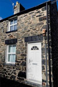 een stenen gebouw met een witte deur en twee ramen bij Cosy Cottage, Nr Betws y Coed. in Llanrwst