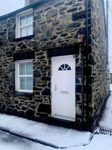 um edifício de pedra com uma porta branca e duas janelas em Cosy Cottage, Nr Betws y Coed. em Llanrwst