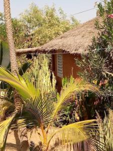 una pequeña casa con techo de paja y algunas palmeras en Résidence Le Marlodj en Mar Lodj