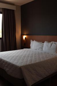 um quarto com uma cama grande com lençóis brancos e uma janela em Comfort Hotel Presidente Prudente em Presidente Prudente