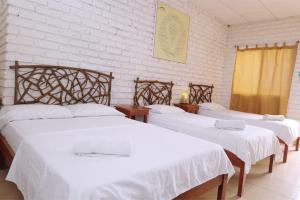 um quarto com três camas com lençóis brancos em Hostal Maresia em Data de Posorja
