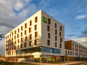 a large white building with a green sign on it at Ibis Styles Montpellier Aéroport Parc Des Expos in Mauguio