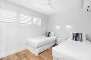 two beds in a room with white walls and wood floors at Commodore Apartment 5, Noosa Heads in Noosa Heads