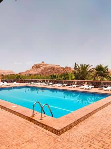 a large swimming pool with chairs and mountains in the background at Hôtel LAKASBAH Ait Ben Haddou in Aït Ben Haddou