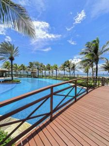 a swimming pool with palm trees and a wooden boardwalk at Golf Ville Resort Residence Bloco 64mar Apto 31 Aquiraz - Ceara - Brasil in Aquiraz