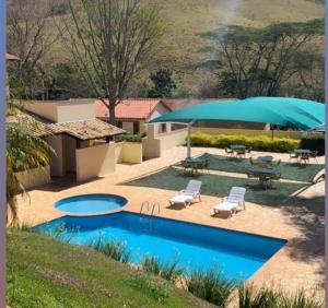 a swimming pool with two chairs and a blue umbrella at Recanto dos Beija flores, Chalé lantana b in Monte Alegre do Sul