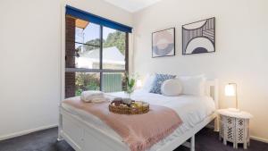 a white bedroom with a bed with a basket on it at Maison de Celine in Bowral