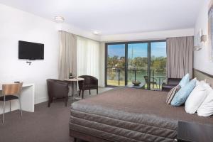a hotel room with a bed and a desk and a balcony at Macquarie 4 Star in Warners Bay