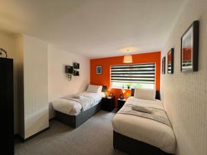 a bedroom with two beds and an orange wall at Havenwood House - Serene Escape Cottage in Nottingham