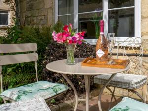 a table with a vase of flowers and a bottle of wine at Pass the Keys Delightful Millend Cottage with Parking and Patio in Northleach