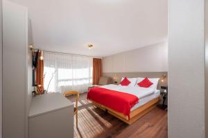Habitación de hotel con cama con sábanas rojas y escritorio. en Hotel Alex Business & SPA en Naters