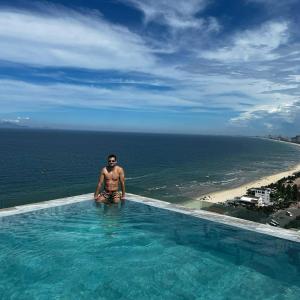 a man sitting in a swimming pool next to the ocean at Alacarte Luxury Ocean View Condotel in Da Nang