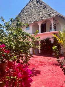 uma casa com telhado de palha e flores cor-de-rosa em Villa Euphoria - Adults Only em Paje