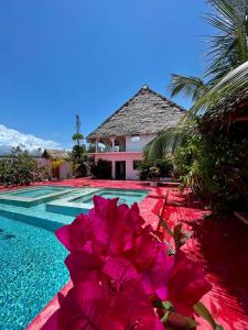 een zwembad met roze bloemen naast een huis bij Villa Euphoria - Adults Only in Paje