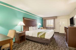 Habitación de hotel con cama, escritorio y TV. en Quality Inn Tulsa Central, en Tulsa