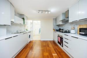 a kitchen with white cabinets and a wooden floor at 2 Bedroom House by AV Stays Short Lets Croydon With Free Wi-Fi in South Norwood