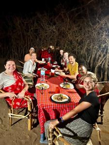 un grupo de personas sentadas alrededor de una mesa comiendo comida en Maasai Eco Boma & Lodge - Experience Maasai Culture en Makuyuni