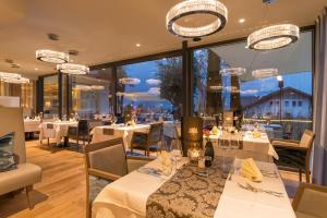 um restaurante com mesas e cadeiras brancas e janelas grandes em Preidlhof Luxury Dolce Vita Resort em Naturno