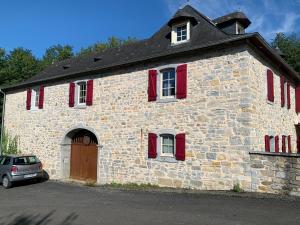 - un bâtiment en pierre avec des volets rouges et une voiture garée devant dans l'établissement Moulin d’Eysus - Le Moulin, à Eysus