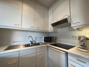 uma cozinha com armários brancos, um lavatório e um micro-ondas em Sfeervol Appartement met Zeezicht em Middelkerke