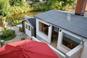 uma pequena casa com um guarda-chuva vermelho ao lado de um rio em Gästehaus Kajüte direkt am Wasser em Friedrichstadt