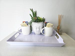 a tray with two cups and a vase with a plant at Sea Breeze Manor - Aqua Unit in East London