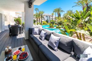 a couch on a balcony with a pool and palm trees at Luxurious Beachside in the Heart of Puente Romano in Marbella