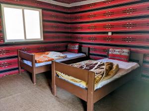 two beds in a room with a red wall at Wadi Rum Camp & Jeep Tour in Wadi Rum