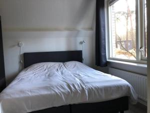 een slaapkamer met een wit bed en een raam bij Vakantiehuis de Eekhoorn in Nunspeet op de Veluwe in Nunspeet