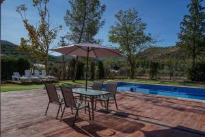 una mesa con sillas y una sombrilla junto a la piscina en La Masía casa rural junto al río, en Almedinilla