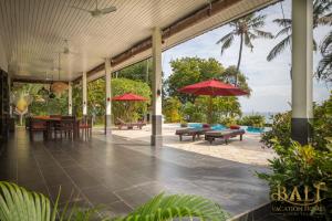 um pátio com mesas, cadeiras e guarda-sóis em Villa Burung, Breathtaking oceanfront, infinity pool 3BR em Tegallengah