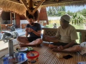 two men sitting on a porch looking at their cell phones at D' Carasti Bungalow in Masbagik