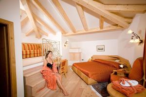 a woman in a dress sitting in a bedroom at Lady Maria Hotel Wellness & Resort in Fondo