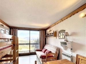 a living room with a couch and a large window at Studio cosy skis aux pieds avec balcon et piscine chauffée - FR-1-267-205 in Le Corbier
