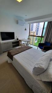 a bedroom with a bed and a tv and a table at Flat Boa Viagem - Rooftop 470 in Recife