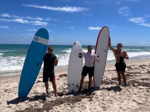 três homens na praia com as suas pranchas de surf em Hutchinson Island Beachfront - 2bd, 2ba Ensuite em Fort Pierce