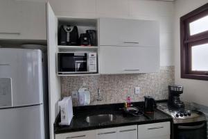 a kitchen with white cabinets and a sink and a microwave at Apto na Bela Lagoa da Conceição in Florianópolis