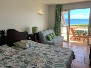 a bedroom with a bed and a chair and a balcony at Studio Cannelle Vue Mer Village Vacances Sainte Anne in Sainte-Anne +51 photos