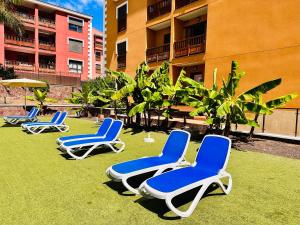 four lounge chairs sitting on the grass in front of a building at Family apartment GRAND in Palm-mar
