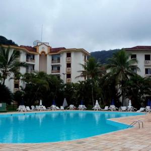 a large swimming pool with chairs and a hotel at Apartamento Condomínio Wembley Tênis - Toninhas - Ubatuba - SP in Ubatuba