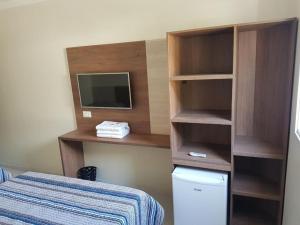 Habitación con cama, TV y estante para libros. en Hotel Guarumar Gold, en Guarujá