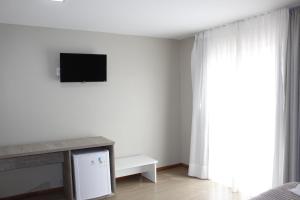 um quarto branco com uma televisão e uma janela em Pousada Essência Serrana Gramado em Gramado