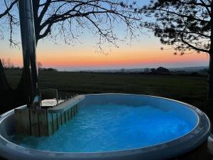 a hot tub in a field with a sunset in the background at La Maisonnette in Saint-Pierre-sur-Dives