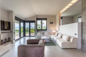 Elle comprend un salon doté d'un mobilier blanc et de grandes fenêtres. dans l'établissement Villa Roccolo, à Calmasino