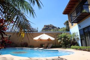 una piscina con sombrilla y sillas junto a una casa en Posada El Canto del Cenzontle, en Tepoztlán